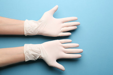 Person in medical gloves on blue background, closeup of handsの写真素材