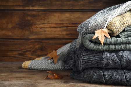 Stack of knitted plaids with dry leaves on wooden table, closeupの写真素材