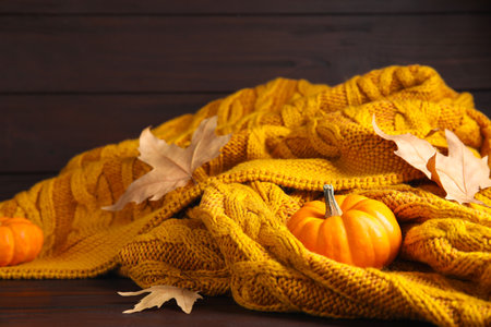 Orange knitted plaid with dry leaves and pumpkins on brown wooden table, closeupの写真素材