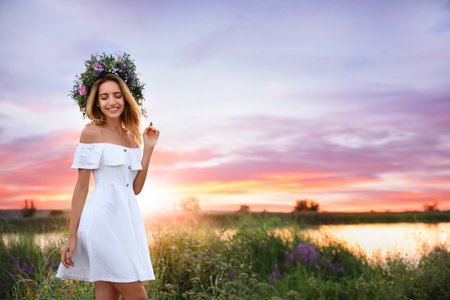 Young woman wearing wreath made of beautiful flowers outdoors at sunsetの写真素材
