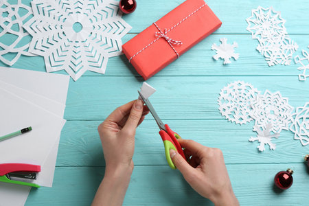 Woman making paper snowflake at turquoise wooden table, top viewの写真素材
