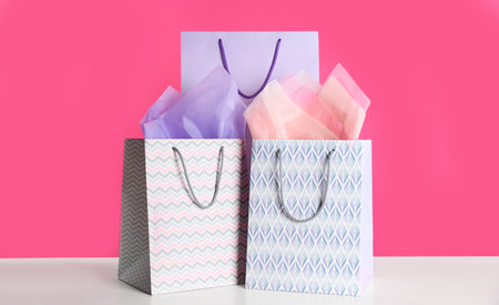 Gift bags with paper on white table against pink backgroundの写真素材