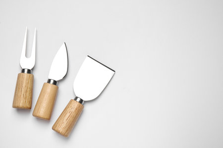 Cheese knives and forks on white background, top view