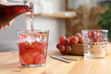 Woman pouring grape soda water into glass at wooden table indoors, closeup. Refreshing drinksの写真素材