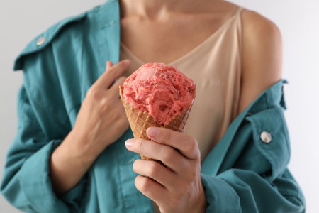 Woman holding pink ice cream in wafer cone on light gray background, closeupの写真素材
