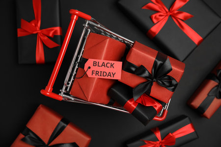 Small shopping cart with wrapped gift boxes on dark background, flat lay. black friday saleの写真素材