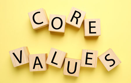 Wooden cubes with phrase CORE VALUES on yellow background, flat lay