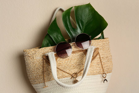 Elegant woman's straw bag with tropical leaf and accessories hanging on beige backgroundの写真素材