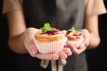 Woman with delicious plum cupcakes on black background, closeupの写真素材