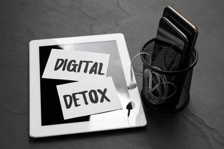 Paper notes with phrase DIGITAL DETOX and different gadgets on black stone tableの写真素材