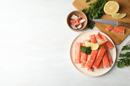 Flat lay composition with crab sticks, knife and lemon on white table, space for textの写真素材