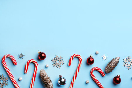 Flat lay composition with candy canes and Christmas decor on light blue background. Space for text