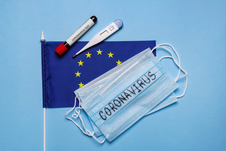 European Union flag, protective masks, thermometer and test tube with blood sample on light blue background, flat lay. coronavirus outbreakの写真素材