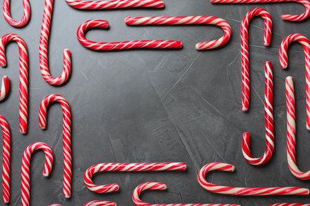 Frame of sweet Christmas candy canes on gray background, flat lay. Space for text