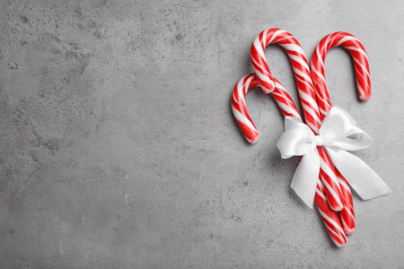 Sweet Christmas candy canes with white bow on gray background, top view. Space for textの写真素材