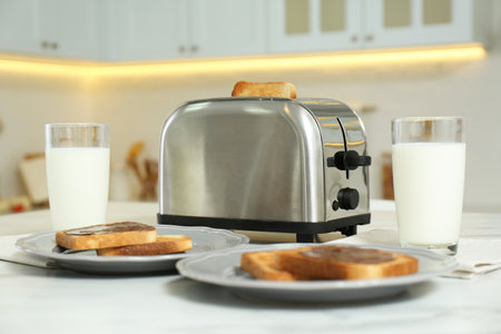 Modern toaster, bread slices with chocolate cream and glasses of milk on white marble table in kitchenの写真素材