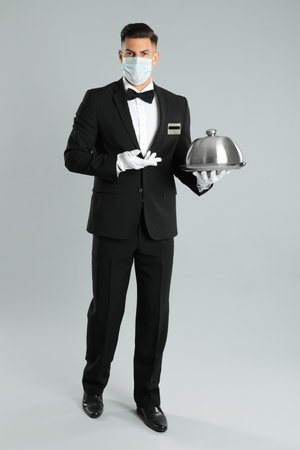 Waiter in medical face mask holding tray on light gray backgroundの写真素材