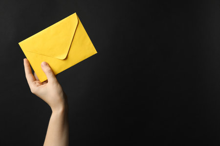 Woman holding yellow paper envelope on black background, closeup. Space for textの写真素材