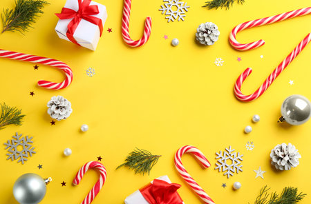 Frame of candy canes and Christmas decor on yellow background, flat lay. Space for textの写真素材