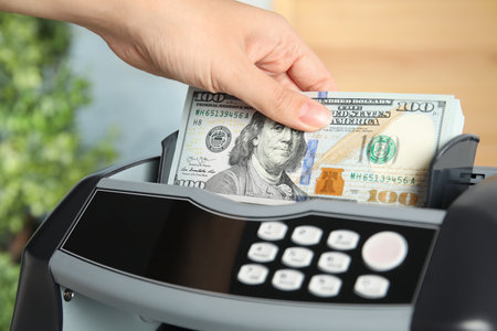Woman putting money into counting machine indoors, closeupの写真素材