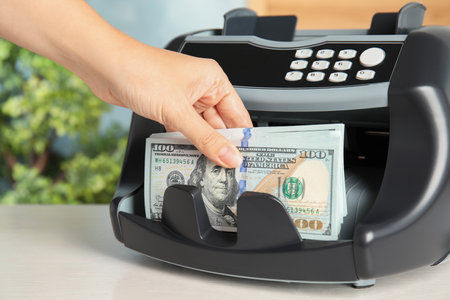 Woman taking money from counting machine at table indoors, closeupの写真素材