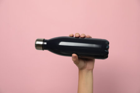 Woman holding modern dark flask on pink background, closeupの写真素材