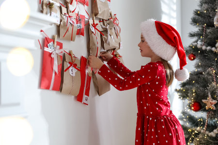 Cute little girl in Santa hat taking gift from Christmas advent calendar at homeの写真素材