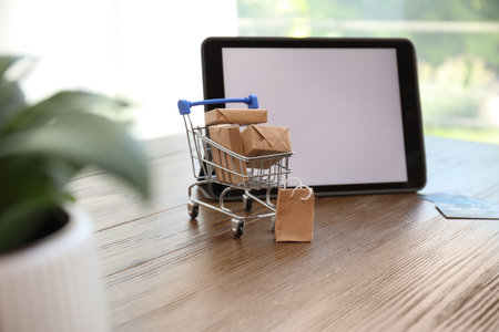 internet shopping. Small cart with boxes and bag near modern tablet on wooden table indoorsの写真素材