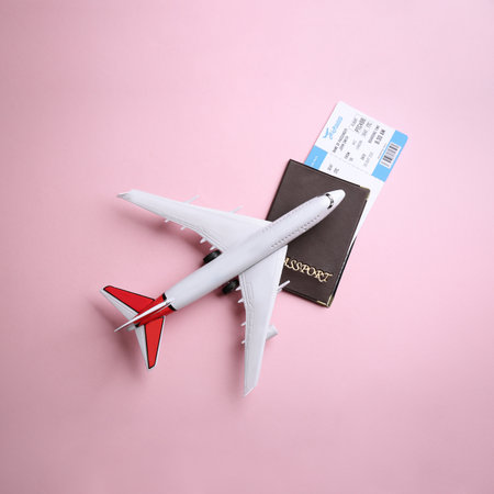 Toy airplane and passport with ticket on pink background, flat lay