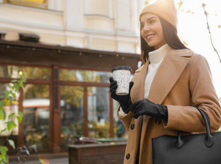 Beautiful young woman with stylish leather gloves and cup of coffee on city streetの写真素材
