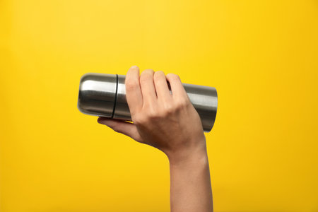 Woman holding modern flask on yellow background, closeupの写真素材
