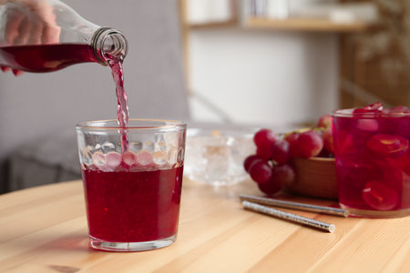 Woman pouring grape soda water into glass at wooden table indoors, closeup. Refreshing drinksの写真素材