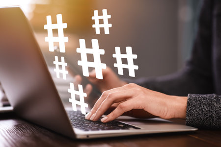 Woman using modern laptop at table, closeup. Hashtag symbols over device