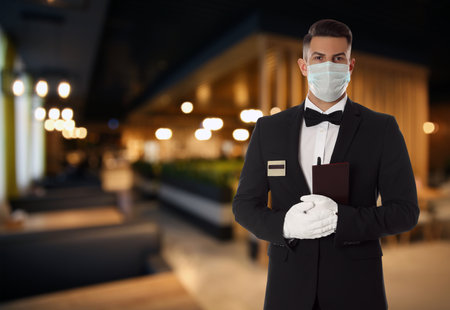 Waiter in medical face mask holding notebook at outdoor cafeの写真素材