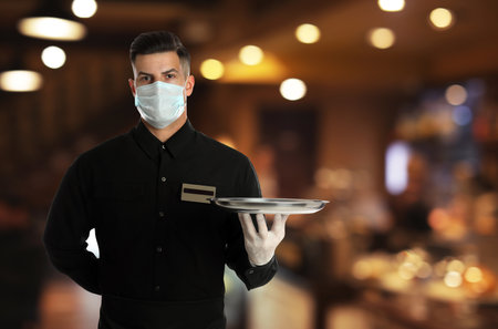 Waiter in medical face mask holding tray in restaurantの写真素材