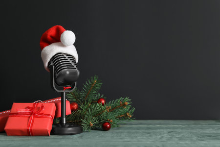 Retro microphone with Santa hat, gift boxes and festive decor on wooden table against black background, space for text. christmas musicの写真素材