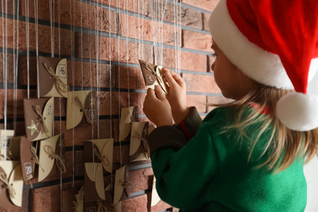 Little girl in Santa hat opening gift from New Year advent calendar indoors, closeupの写真素材