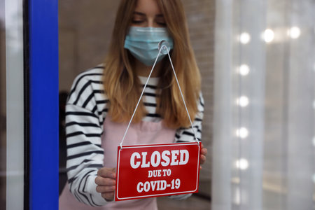 Business owner in mask hanging red sign with text Closed Due To Covid-19 onto glass door. Coronavirus quarantineの写真素材