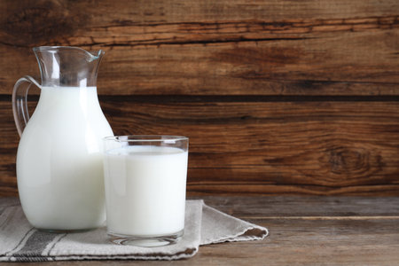 Jug and glass with fresh milk on wooden table. Space for textの写真素材