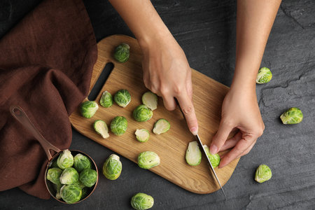Woman cutting Brussels sprout at black slate table, top viewの写真素材
