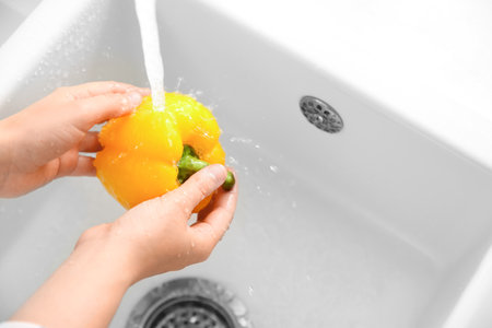 Woman washing fresh yellow bell pepper in kitchen sink, closeup. Space for textの写真素材