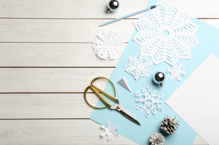 Flat lay composition with paper snowflakes, scissors and Christmas decoration on white wooden background, space for textの写真素材