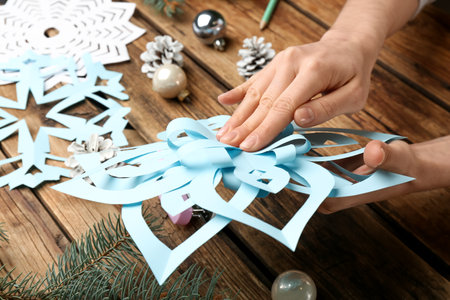 Woman making paper snowflake at wooden table, closeupの写真素材