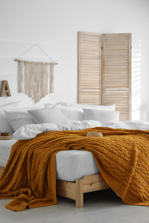 Comfortable bed with warm knitted plaid in stylish room interiorの写真素材
