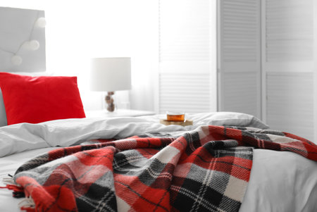 Comfortable bed with warm checkered plaid in stylish room interiorの写真素材