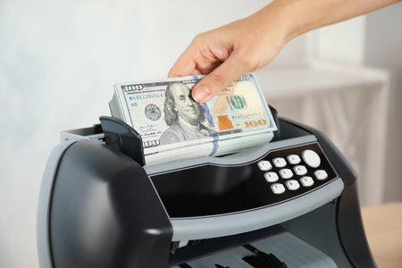 Woman putting money into counting machine indoors, closeupの写真素材