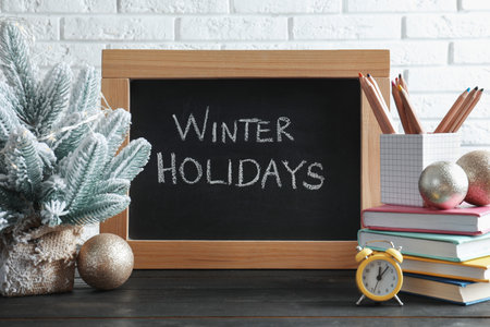 Chalkboard with phrase Winter Holidays, Christmas decor and stationery on black wooden table near white brick wallの写真素材