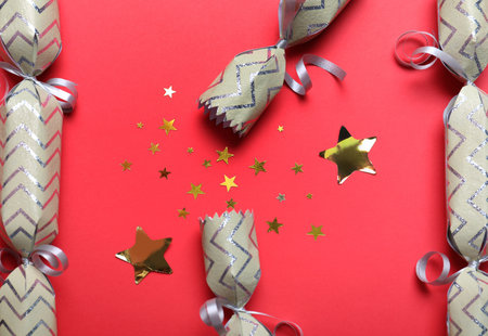 Open and closed Christmas crackers with shiny confetti on red background, flat layの写真素材