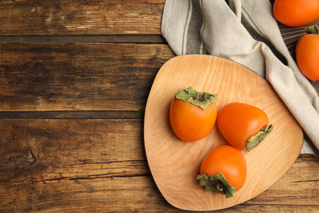 Tasty ripe persimmons on wooden table, flat lay. Space for textの写真素材