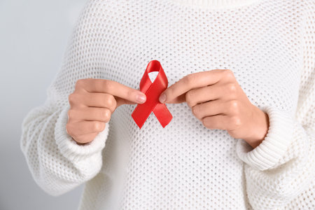 Woman holding red awareness ribbon on light background, closeup. World AIDS disease day